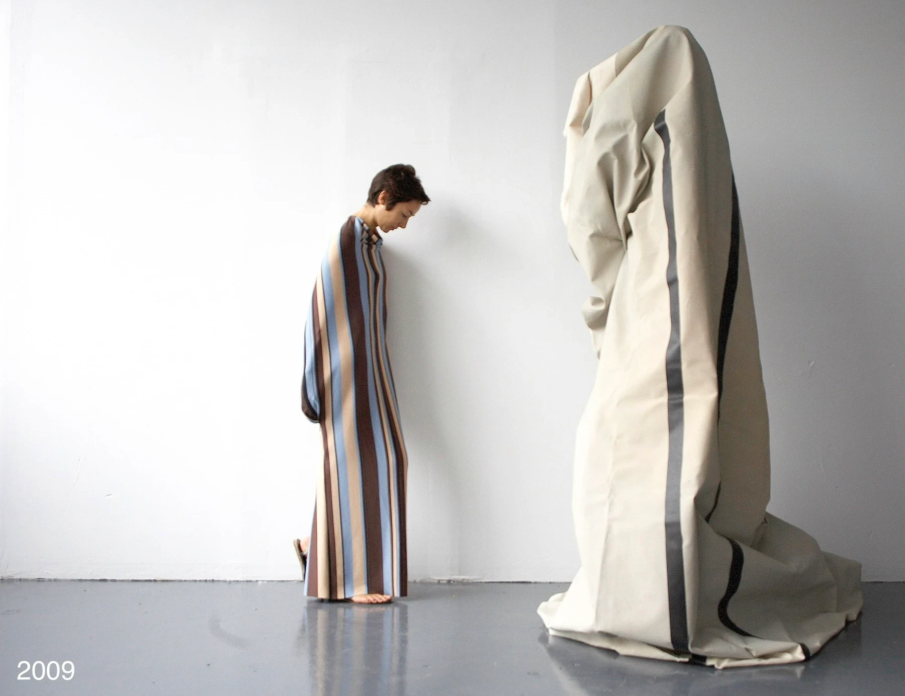 A person in a striped dress beside a tall draped cream form.