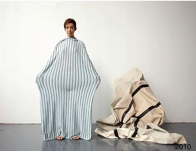 A person in a wide striped garment beside a crumpled tan form.
