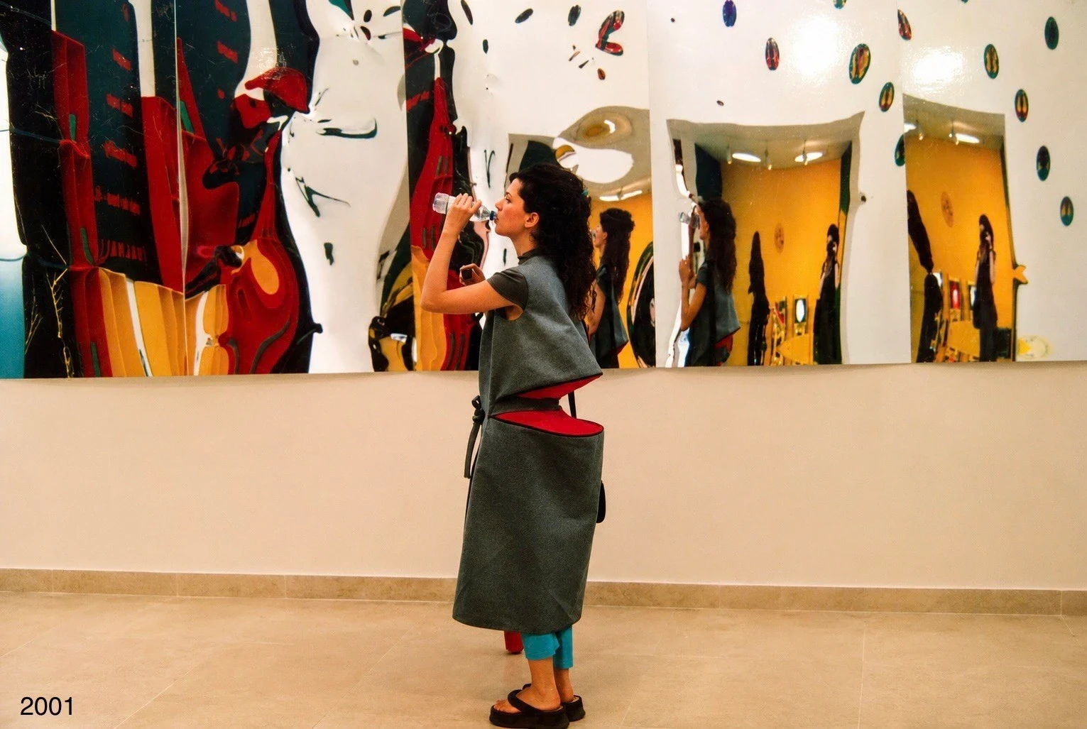A person wearing a dark garment in front of colorful hanging works.