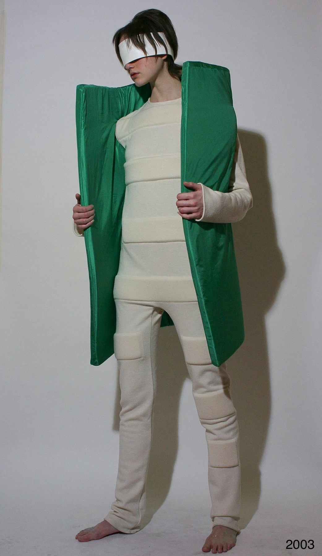 A person in a rectangular green vest over light trousers.