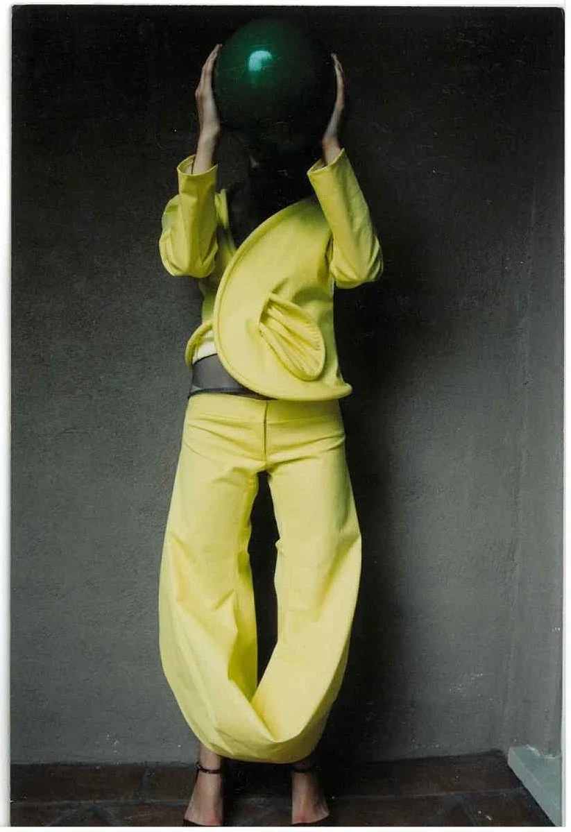 A person wearing a loose yellow outfit and holding a dark round object.
