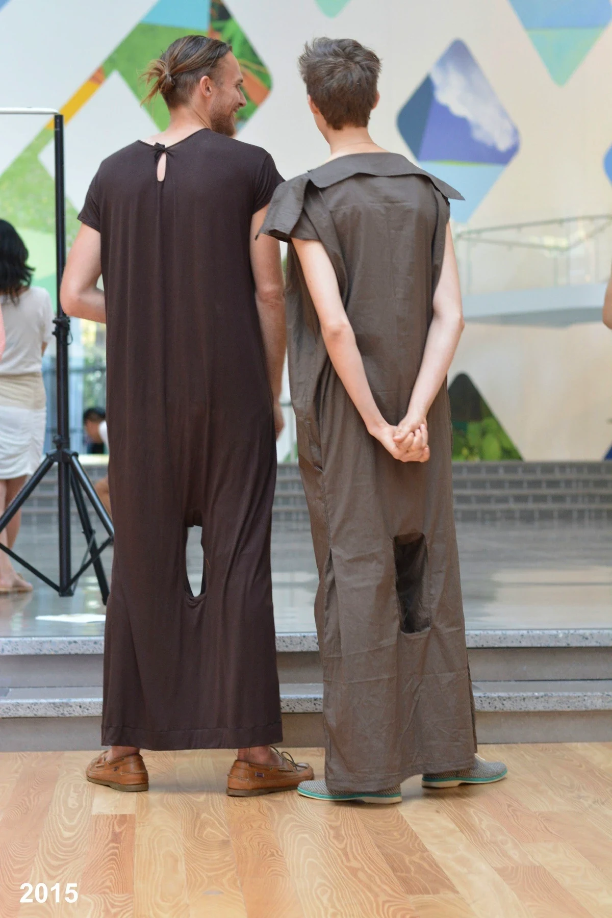 Two people in dark loose garments standing in a studio.