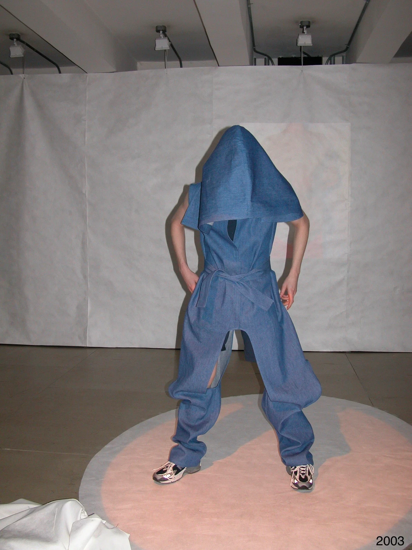 A person in a hooded blue garment with wide folded legs.