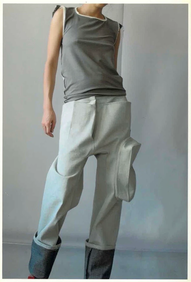 A person in a gray asymmetric top and pale trousers.