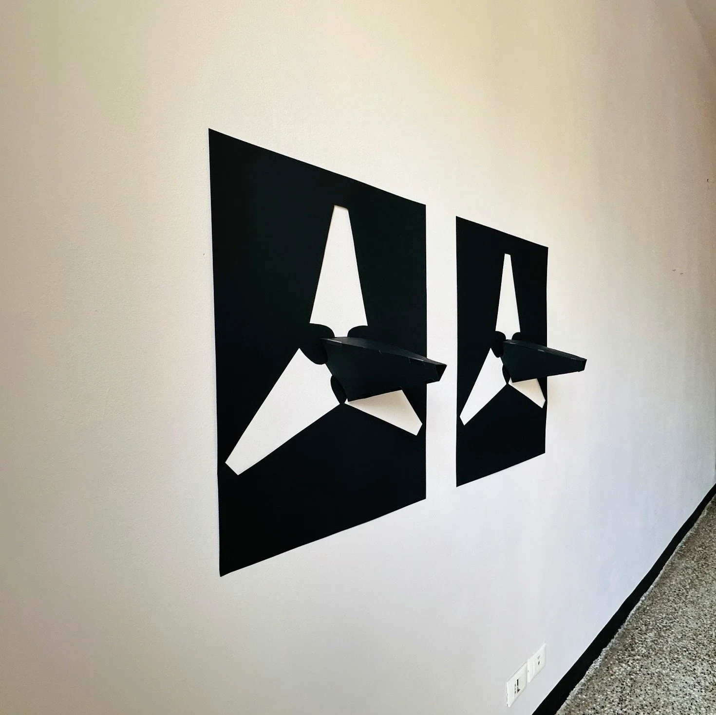 Two black wall works with projecting white and black shapes.