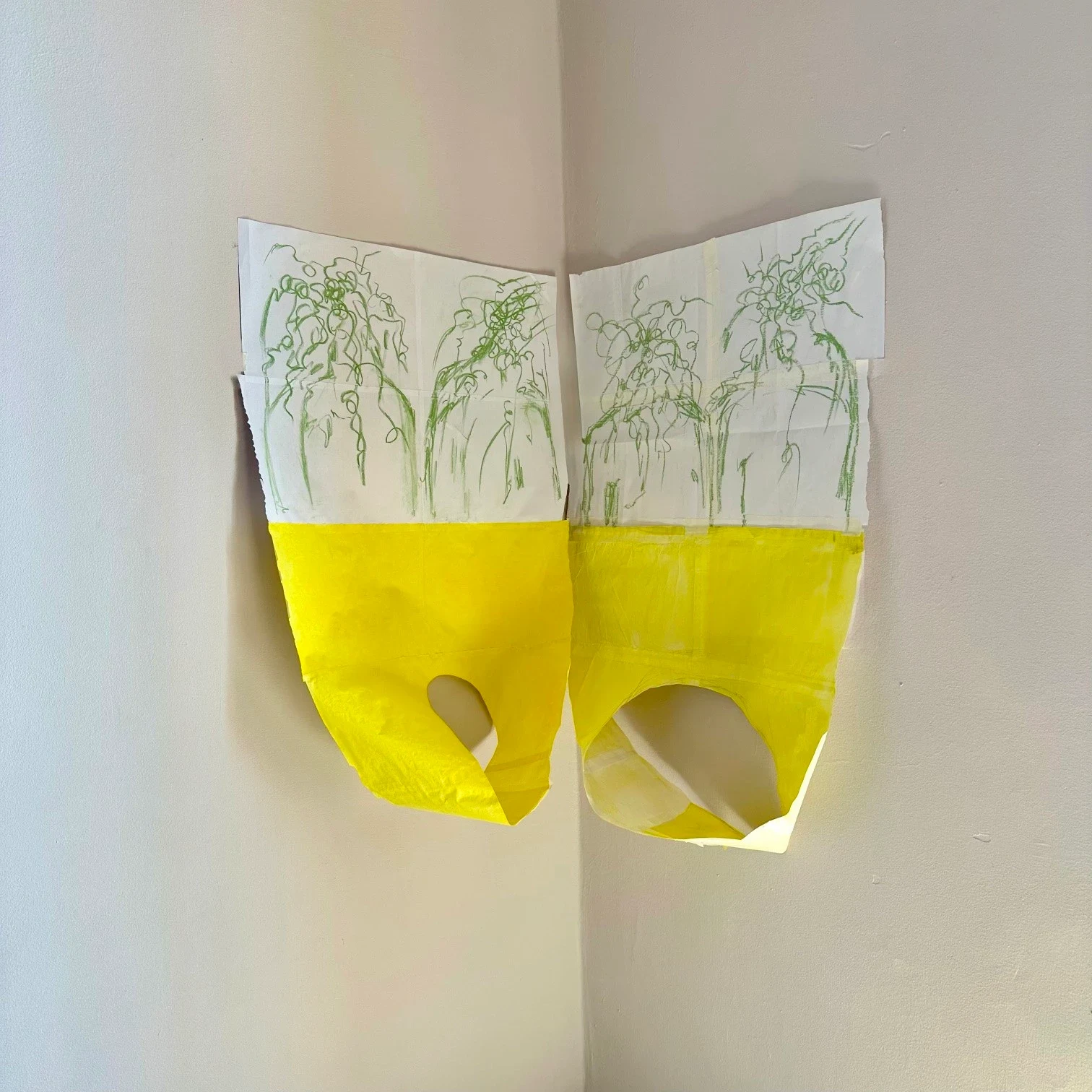 Two curled yellow paper works with green drawings.