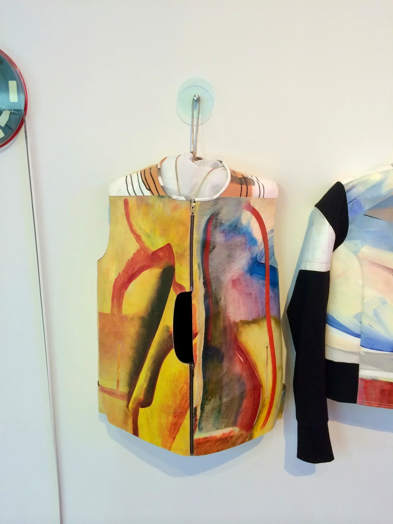 A sleeveless garment made from a colorful painting hanging on a wall.
