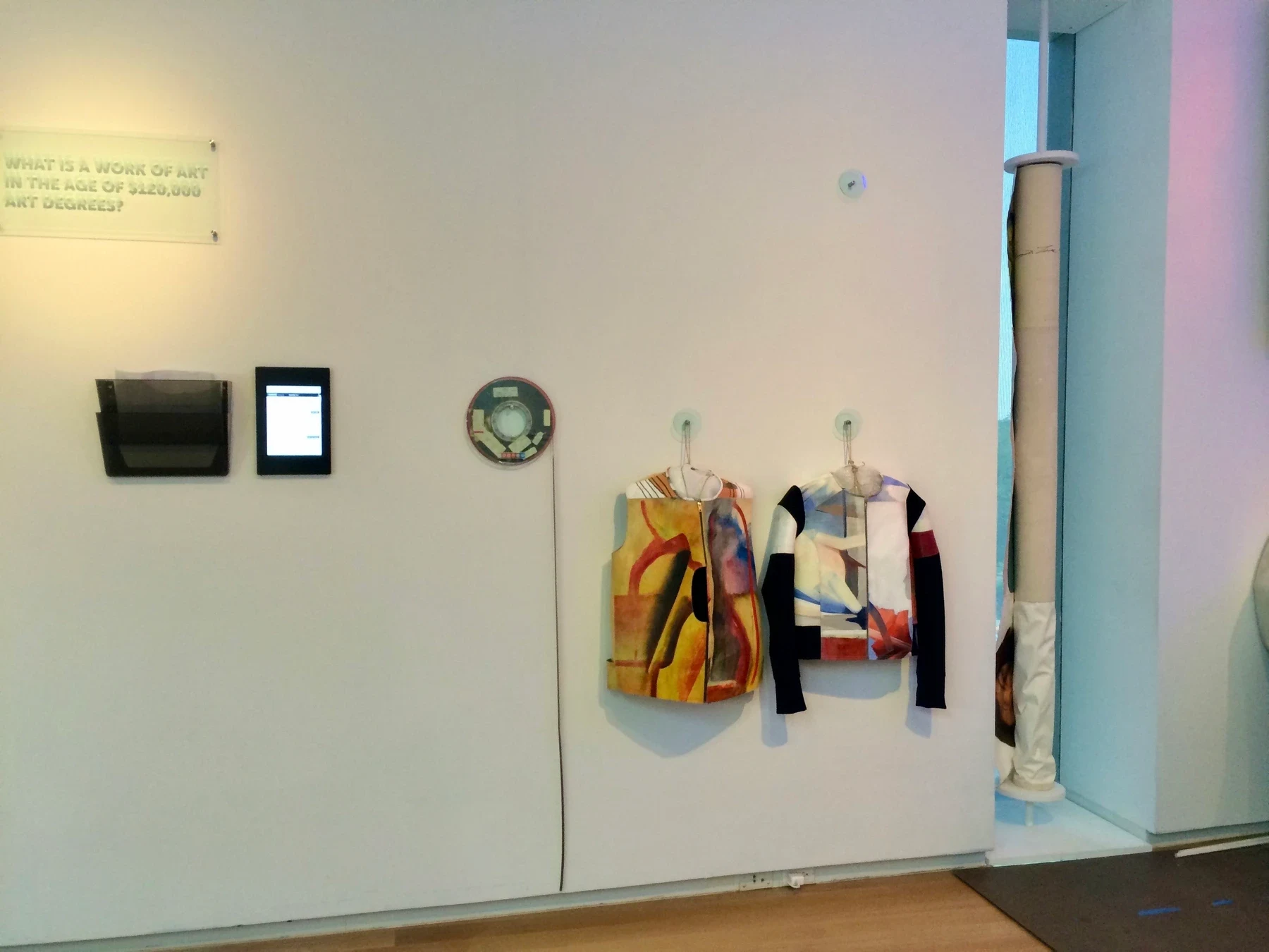 Garments and small works displayed on a white gallery wall.