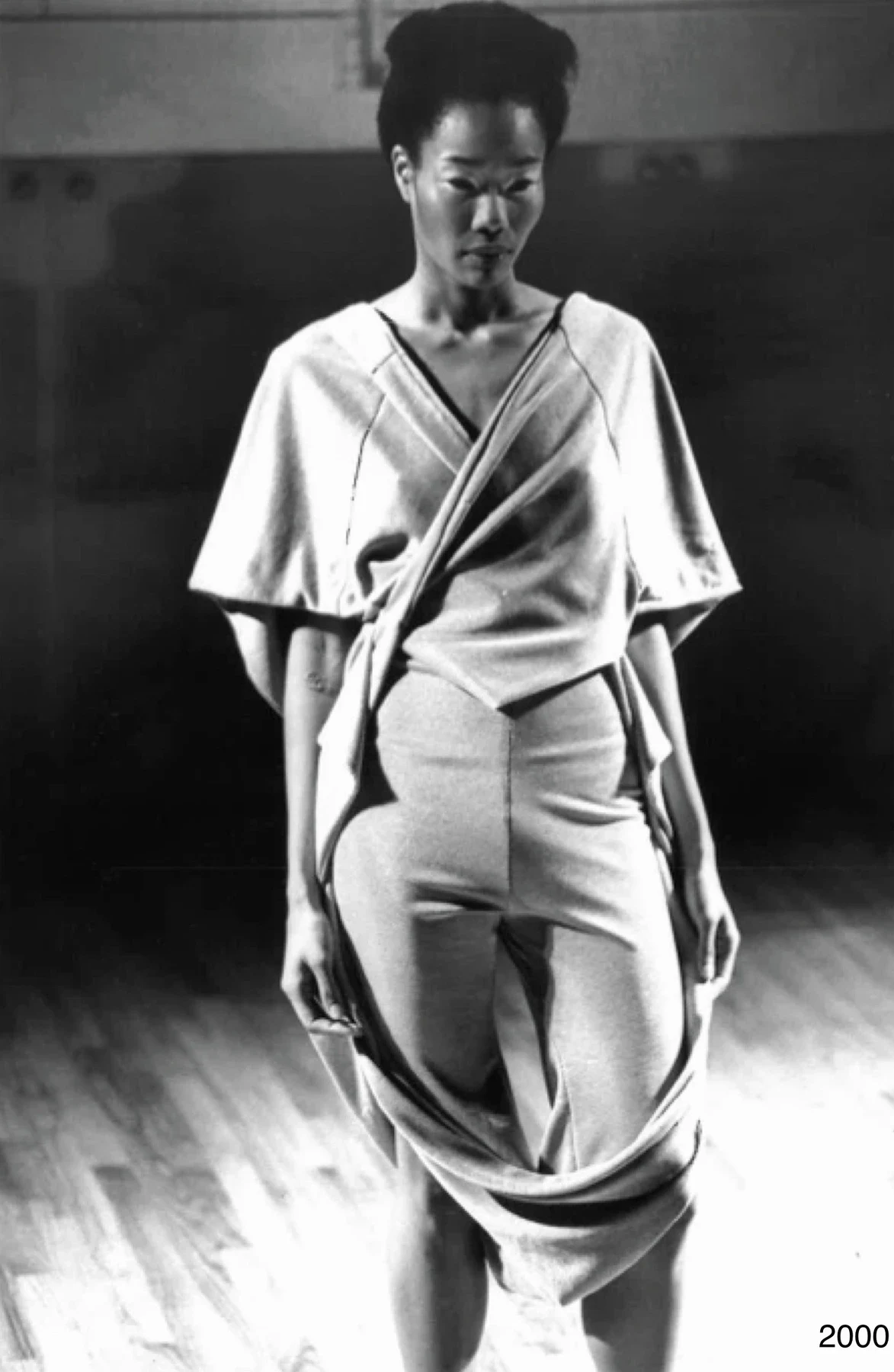 Black and white photograph of a person in an asymmetrically draped outfit.